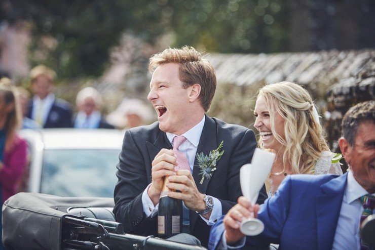 bride and groom laughing as groom pops champagne at a south hams wedding in devon