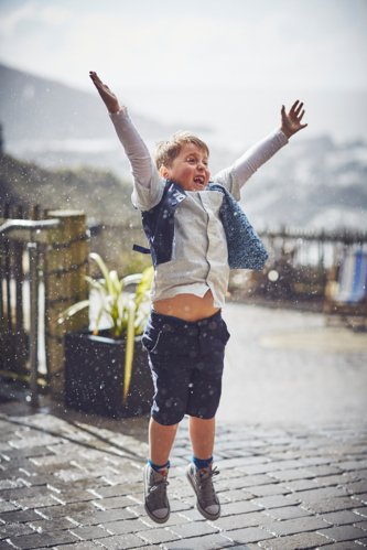 fun wedding photography of boy jumping in rain at tunnels beaches Devon little boy jumping in the rain at Tunnels Beaches Devon