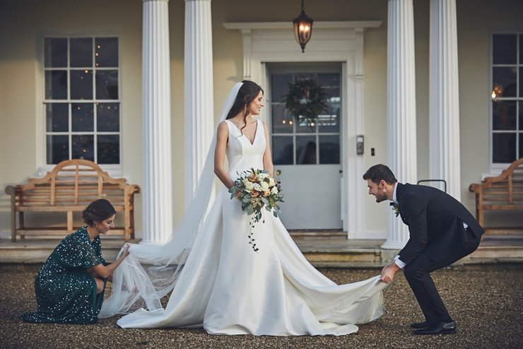 maid of honour and groom adjust brides wedding dress at small winter wedding at Rockbeare manor in Devon