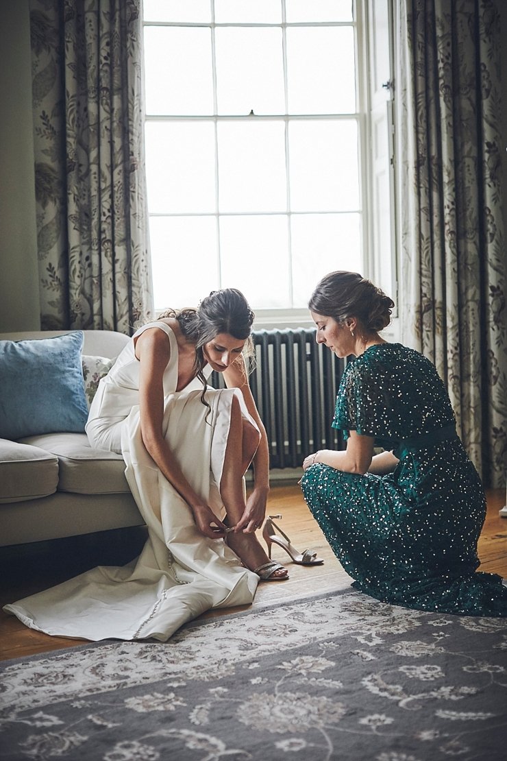 bride putting on her wedding shoes with her bridesmaid at Rockbeare manor in Exeter