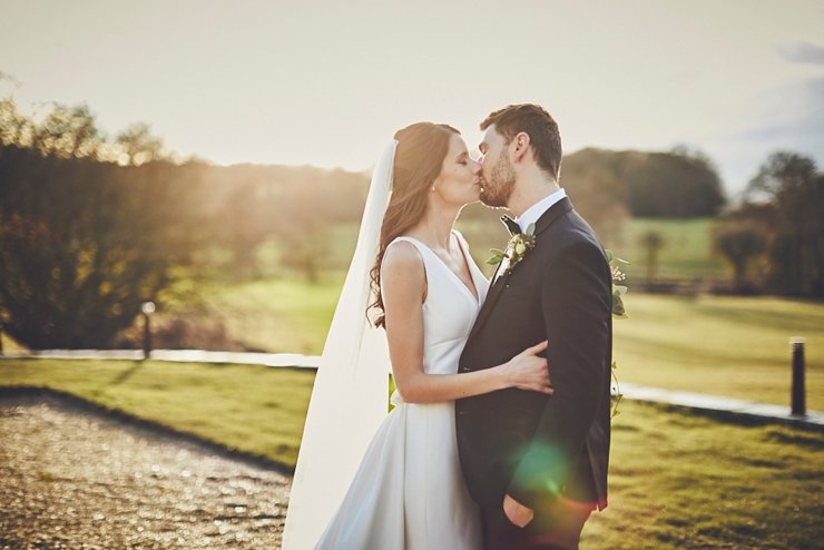 bride and groom kissing in golden hour sunlight at small winter wedding at Rockbeare manor in Devon