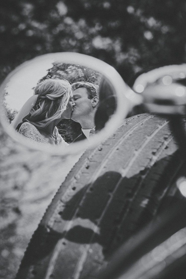 reflection of happy couple kissing in the wing mirror of vintage rolls Royce at a wedding in Devon
