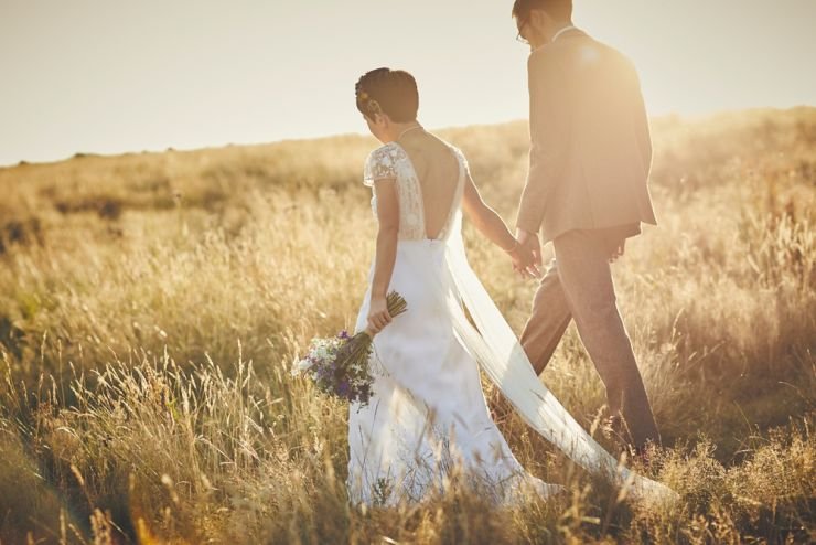 documentary wedding photograph of bride and groom hand in hand walking through corn filed at sunset in devon