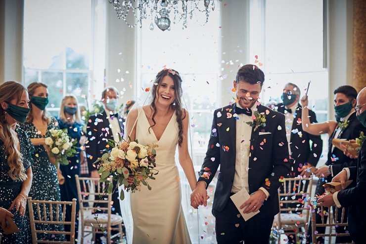 bride and groom walking through indoor confetti shower at small devon wedding at Rockbeare Manor
