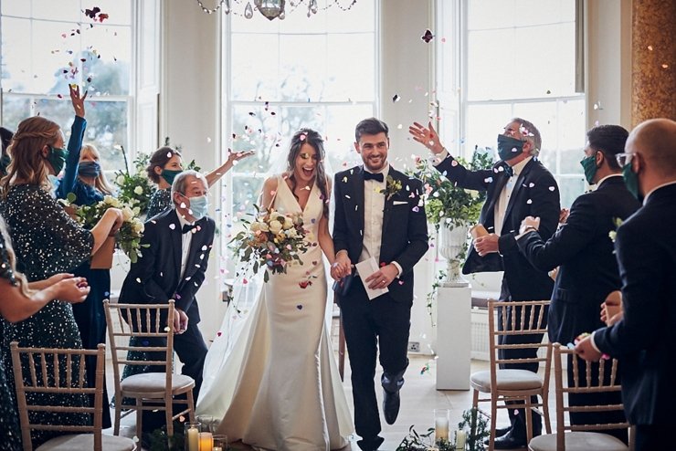 bride and groom walking through indoor confetti shower at small devon wedding at Rockbeare Manor